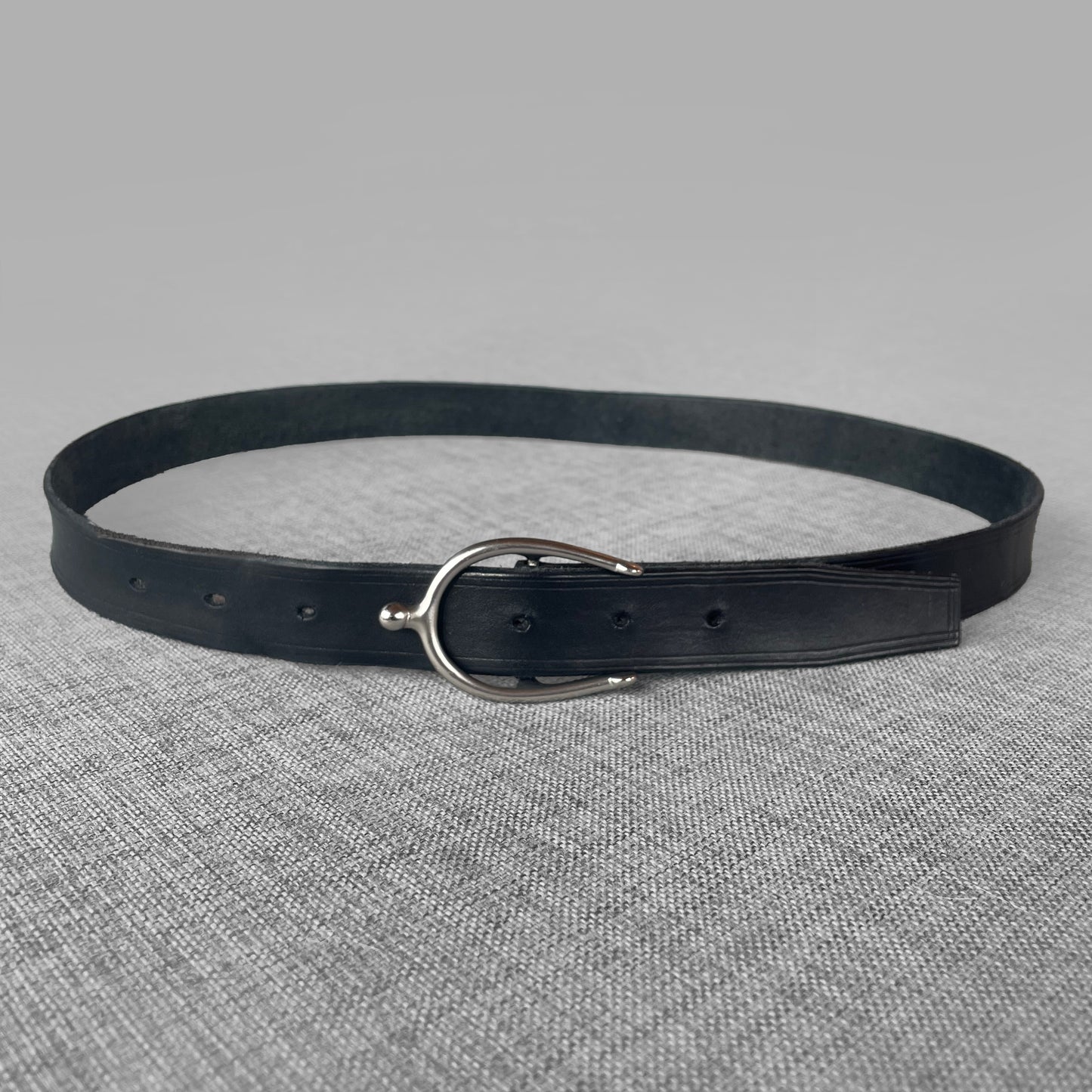 Ceinture en cuir bleu marine enroulee avec boucle argentee en forme de crochet, vue de face