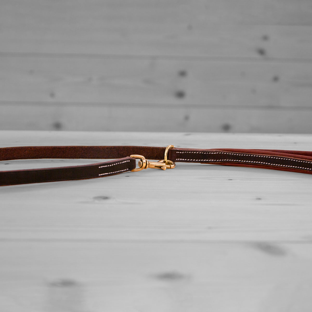 Longe en cuir brun avec mousqueton pivotant en laiton posee sur un plancher en bois