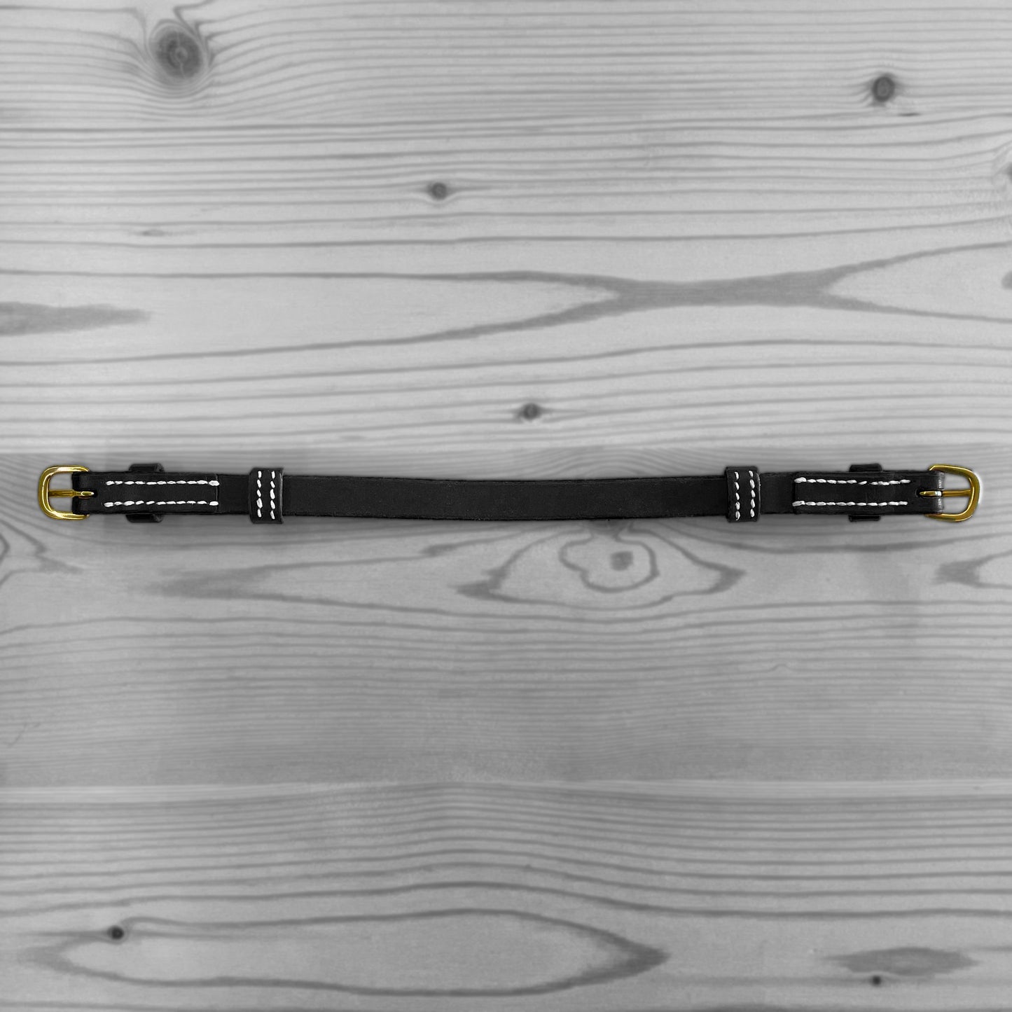 Sangle en cuir noir avec boucles metalliques posee a plat sur un fond de bois