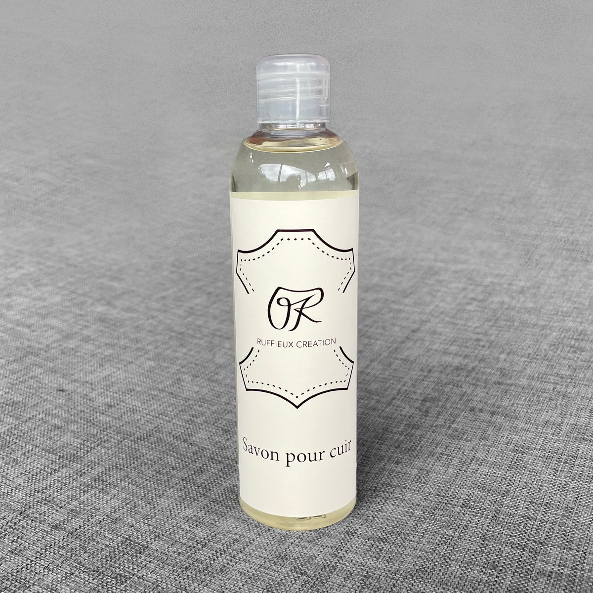 Flacon de savon pour cuir Ruffieux Creation pose sur un fond gris