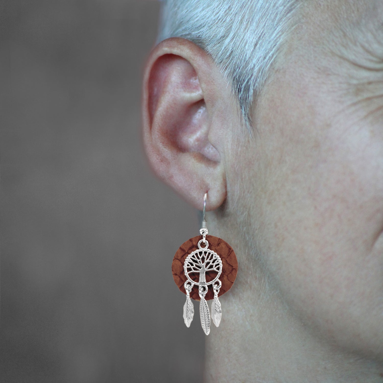 Boucle d'oreille en bois avec arbre de vie et plumes argentees portee a l'oreille