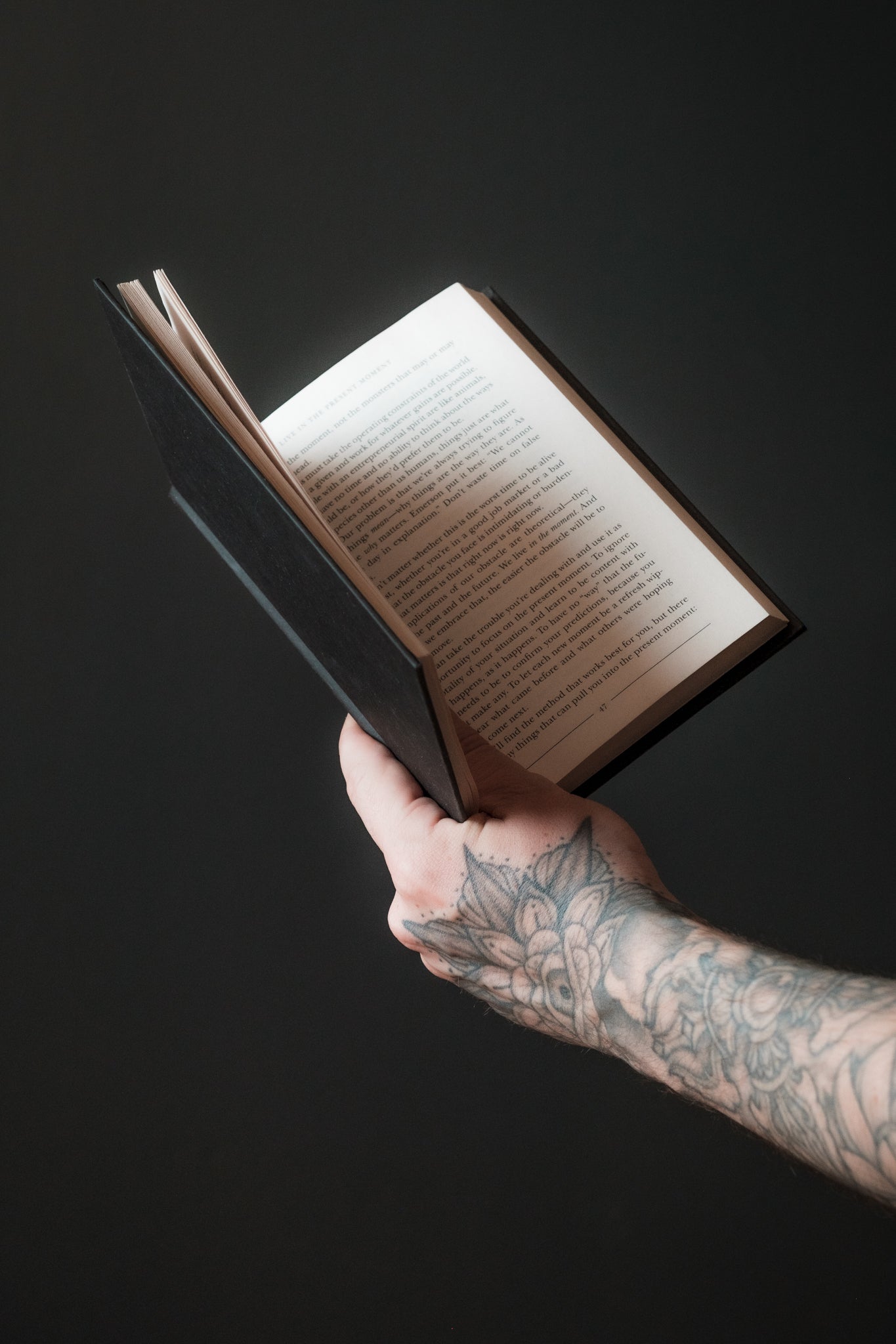 Bras tatoué tenant un livre ouvert sur fond sombre