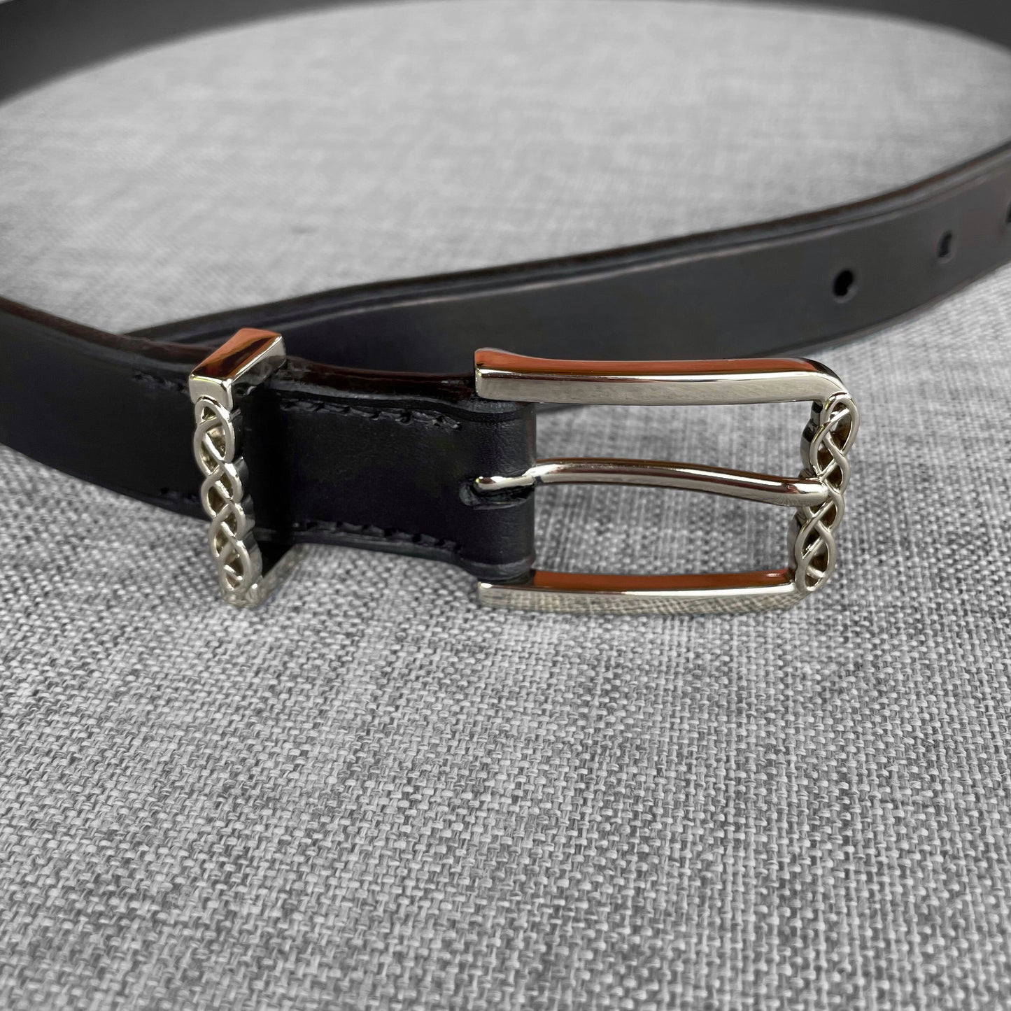 Detail de la boucle argentee tressee d'une ceinture en cuir noir avec doublure brune