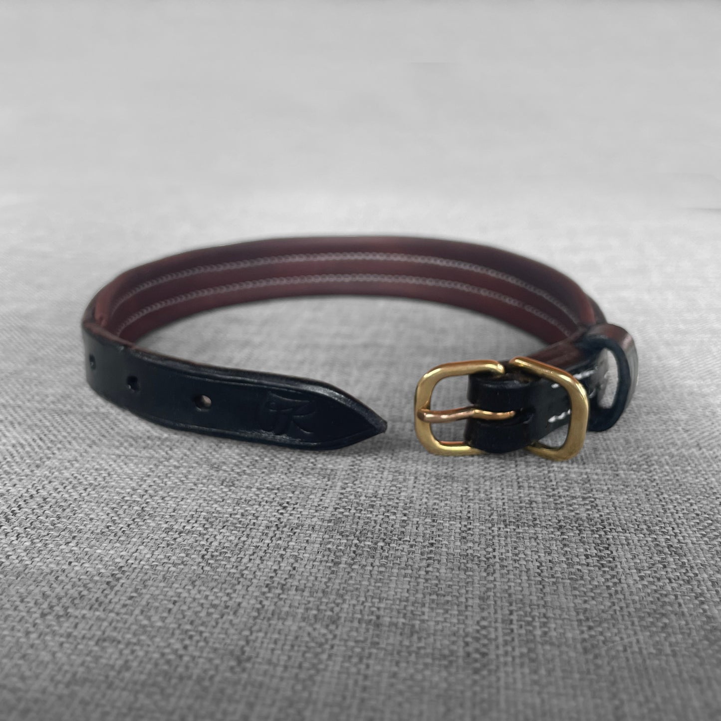 Collier pour chien en cuir noir avec boucle en laiton pose sur un tissu gris