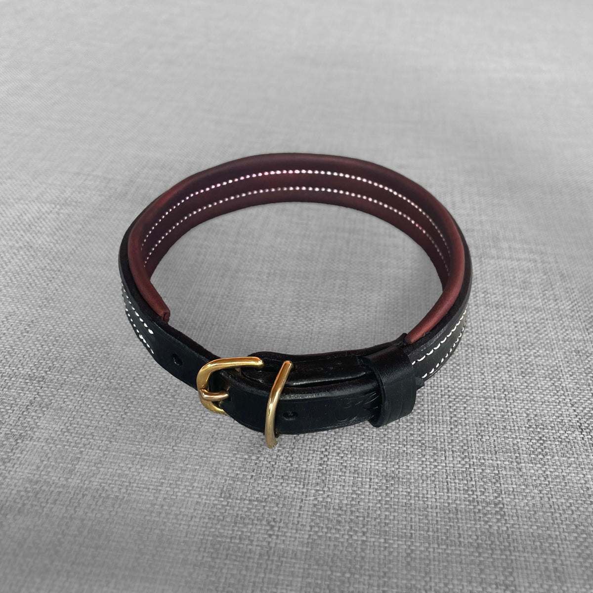 Collier pour chien en cuir noir enroule avec boucle en laiton pose sur un tissu gris