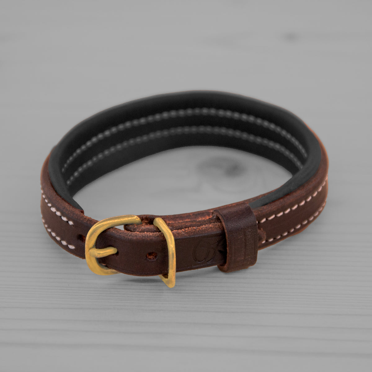 Collier en cuir brun avec doublure noire et boucle en laiton pose sur un plancher en bois