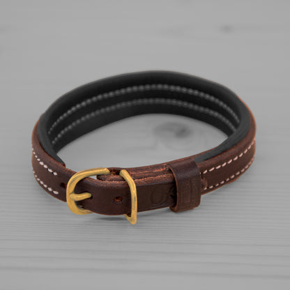 Collier en cuir brun avec doublure noire et boucle en laiton pose sur un plancher en bois