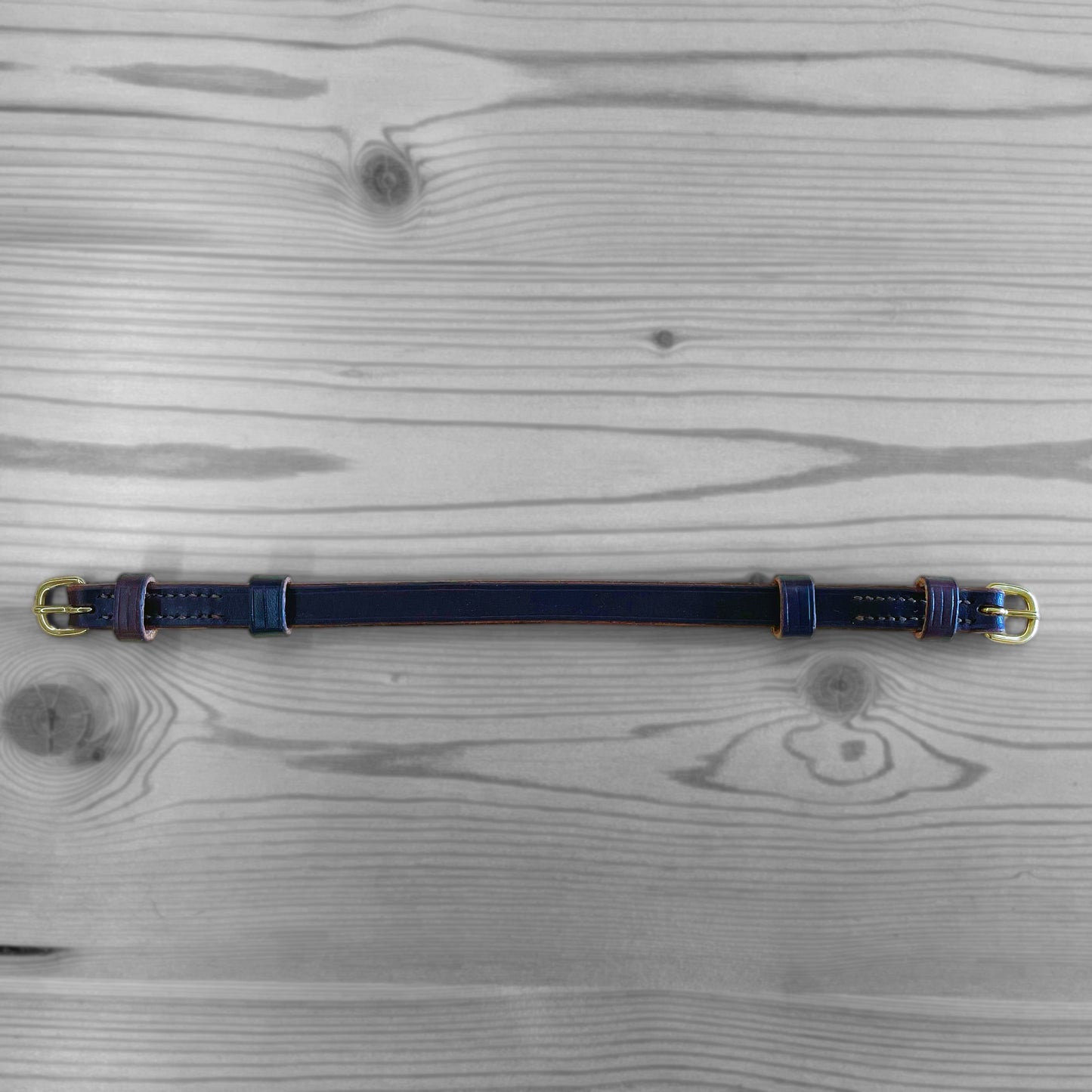 Collier en cuir bleu marine avec boucles dorees pose sur un fond de bois
