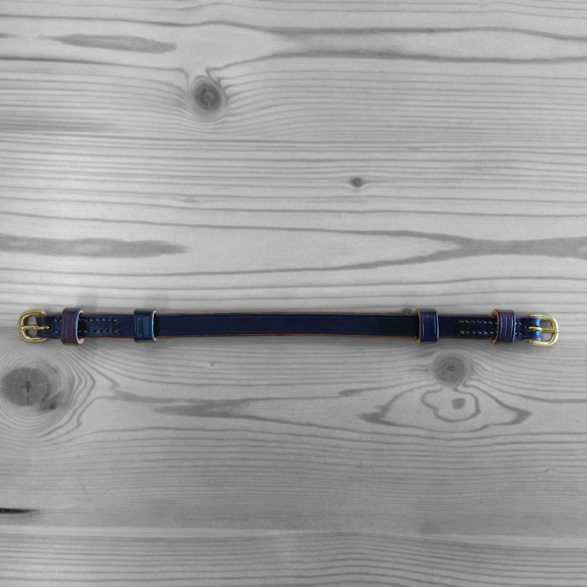 Collier en cuir bleu marine avec boucles dorees pose sur un fond de bois