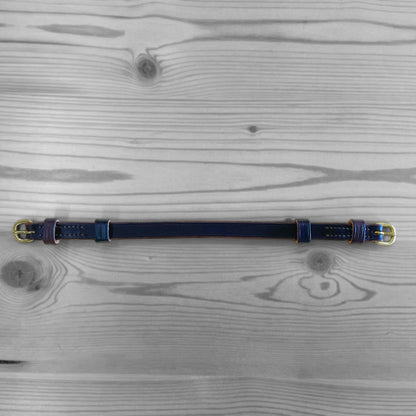Collier en cuir bleu marine avec boucles dorees pose sur un fond de bois