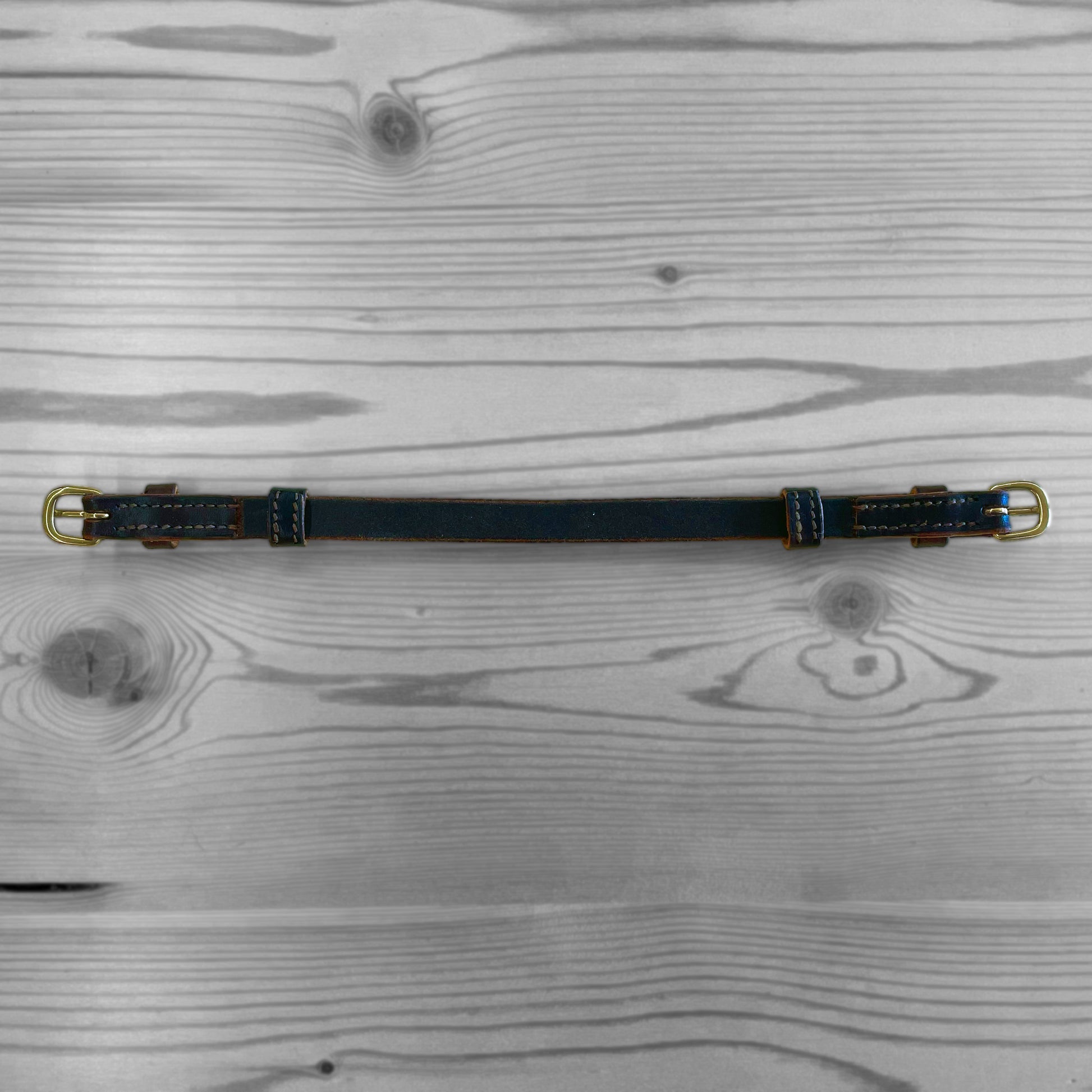 Collier en cuir bleu marine large avec boucles dorees pose sur un fond de bois