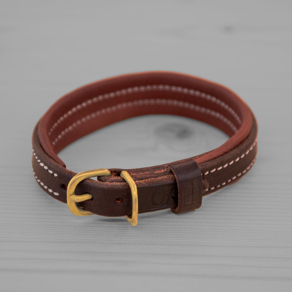 Collier en cuir brun avec boucle en laiton pose sur un plancher en bois