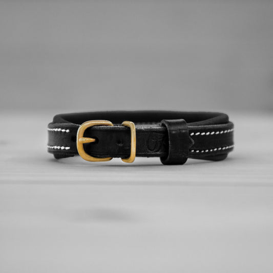 Collier en cuir noir avec boucle en laiton pose debout sur un fond gris