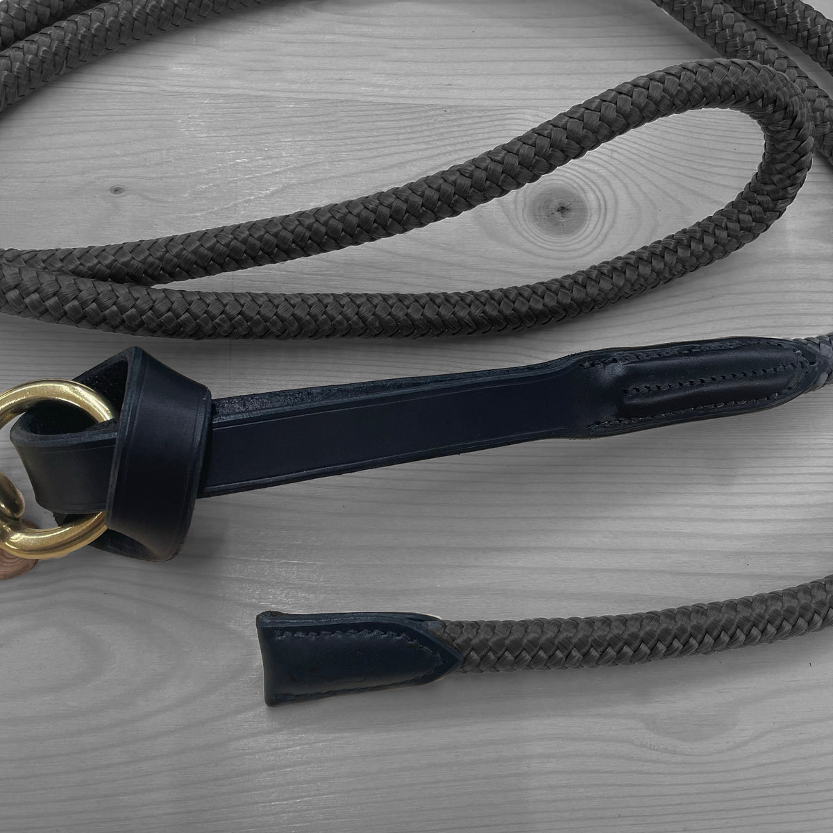 Longe en corde noire avec cuir bleu marine et anneau en laiton posee sur un fond de bois