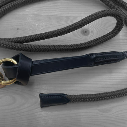 Longe en corde noire avec cuir bleu marine et anneau en laiton posee sur un fond de bois