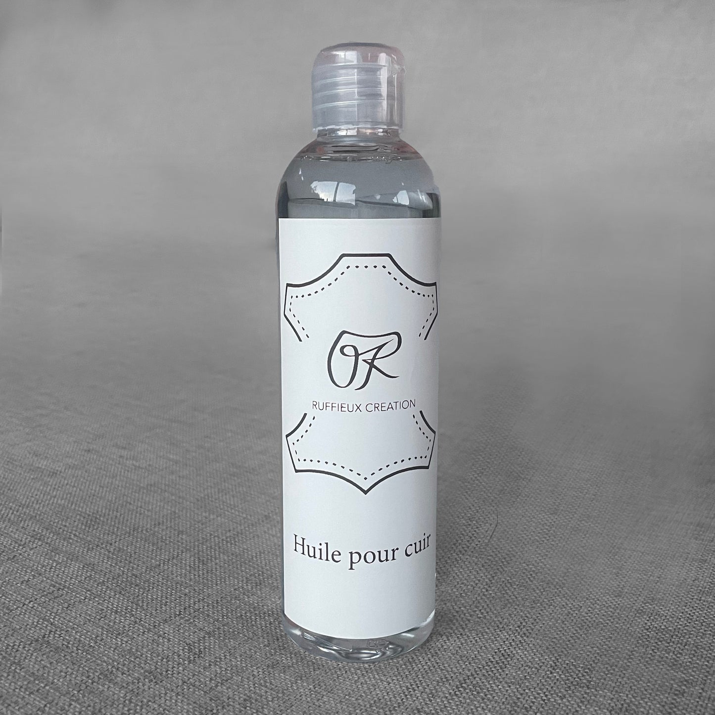 Flacon d'huile pour cuir Ruffieux Creation pose sur un fond gris