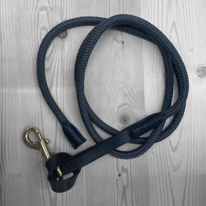 Longe en corde bleu marine enroulee avec mousqueton en laiton sur un fond de bois