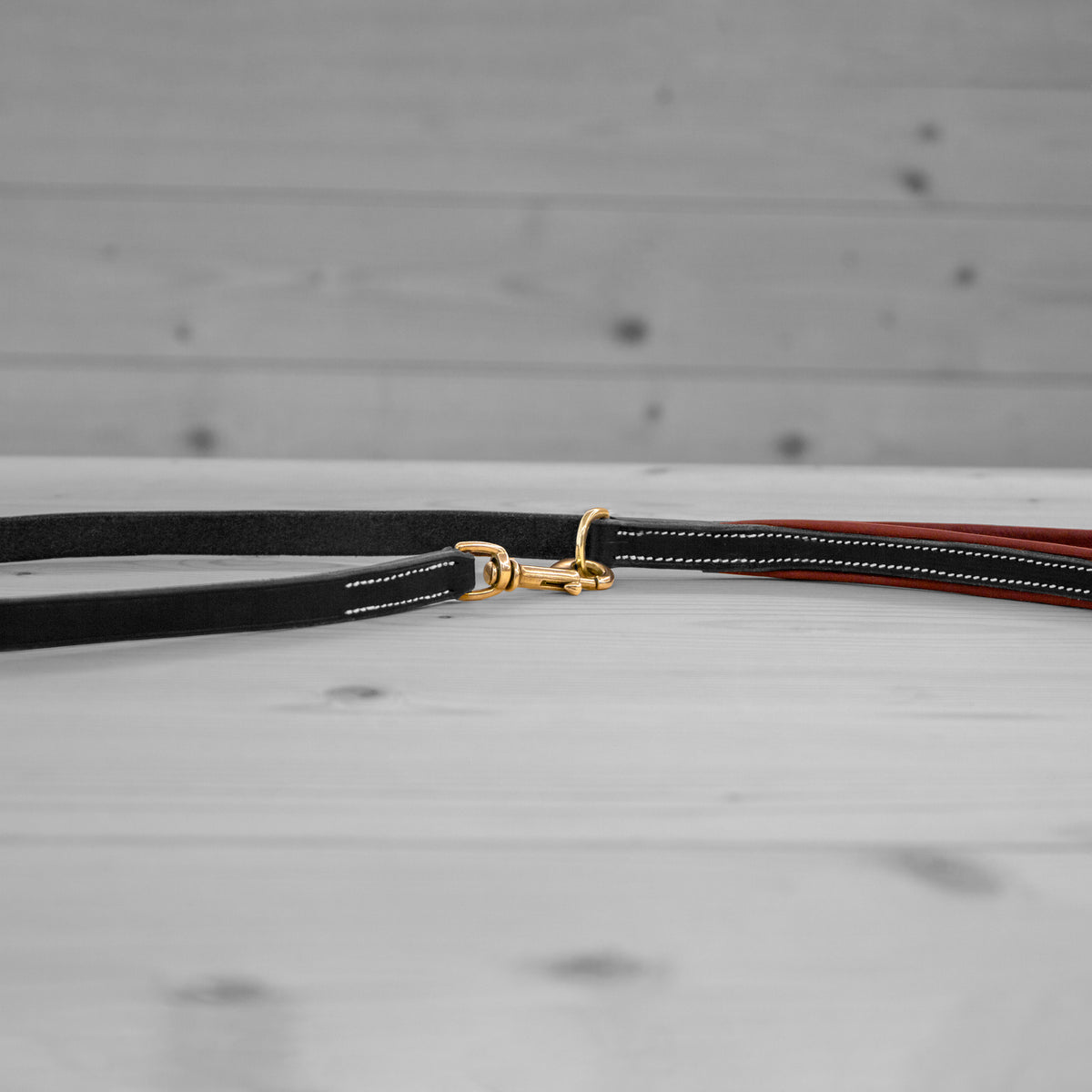Longe en cuir noir avec mousqueton pivotant en laiton posee sur un plancher en bois