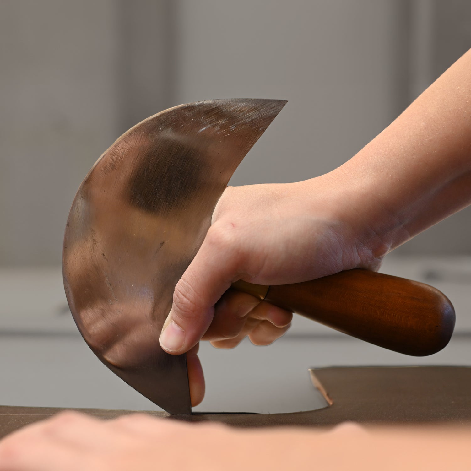 Main d'artisan maniant un couteau rond de sellier pour decouper le cuir