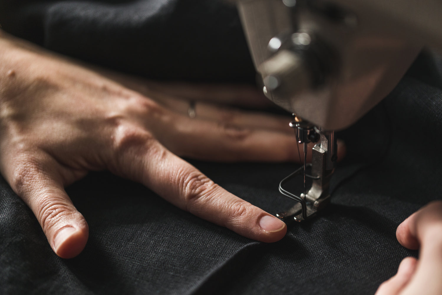 Main guidant un tissu noir sous l'aiguille d'une machine à coudre