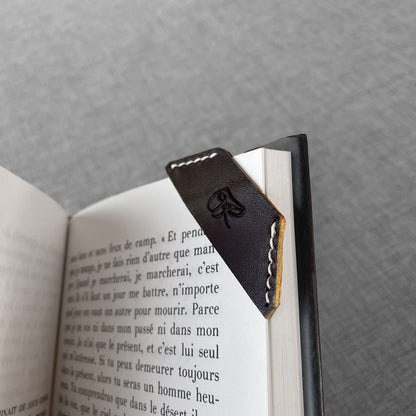 Marque-page en cuir noir avec logo grave, gros plan sur un livre ouvert
