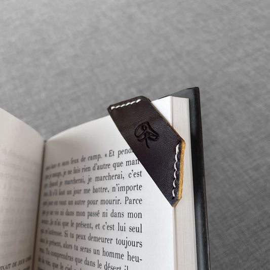 Marque-page en cuir noir avec logo grave, gros plan sur un livre ouvert