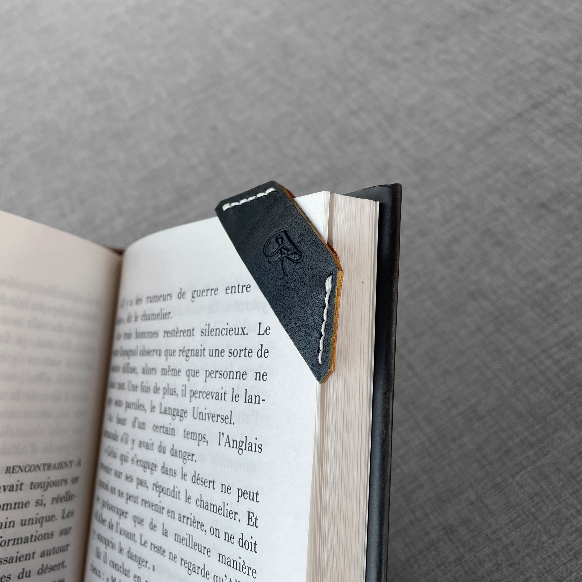 Marque-page en cuir noir avec logo grave pose sur un livre ouvert