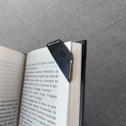 Marque-page en cuir noir avec logo grave pose sur un livre ouvert