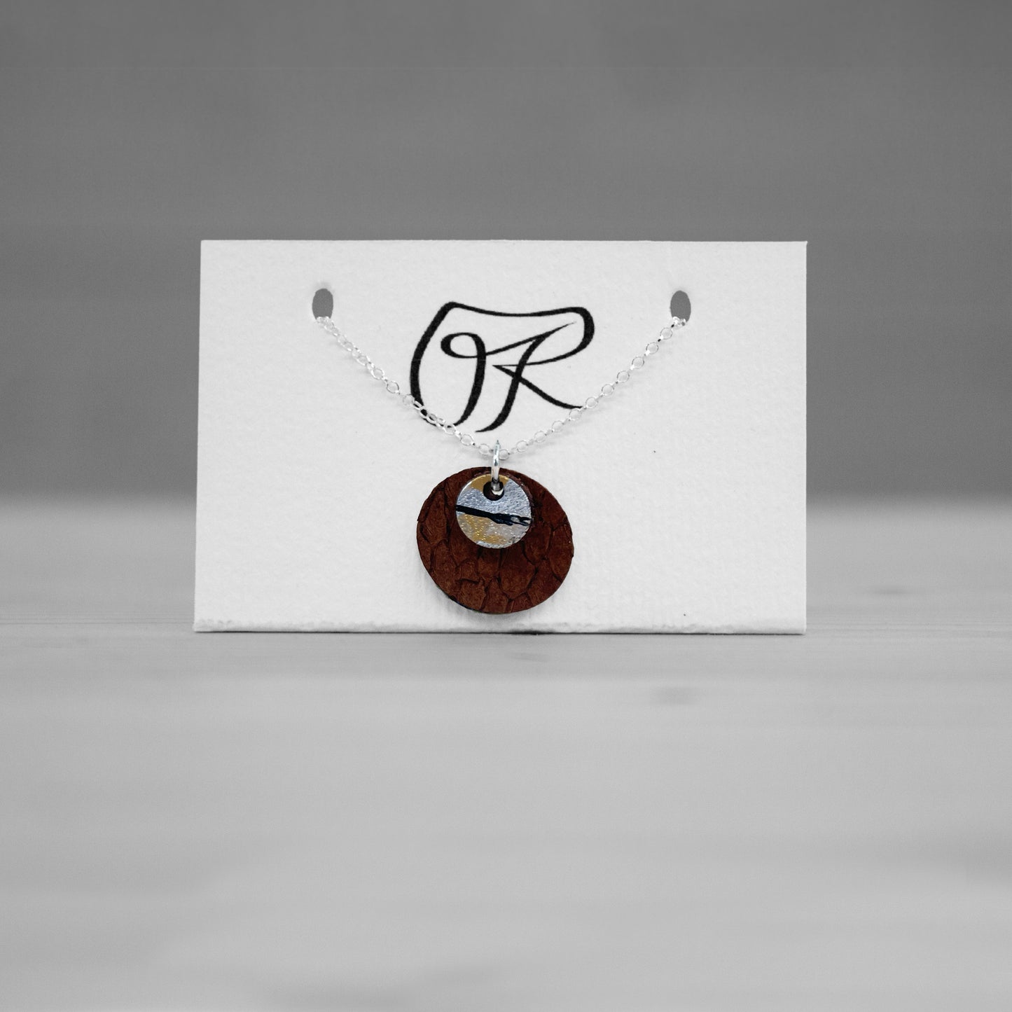 Pendentif rond en cuir brun sur carte de presentation, bijou cuir Ruffieux Creation