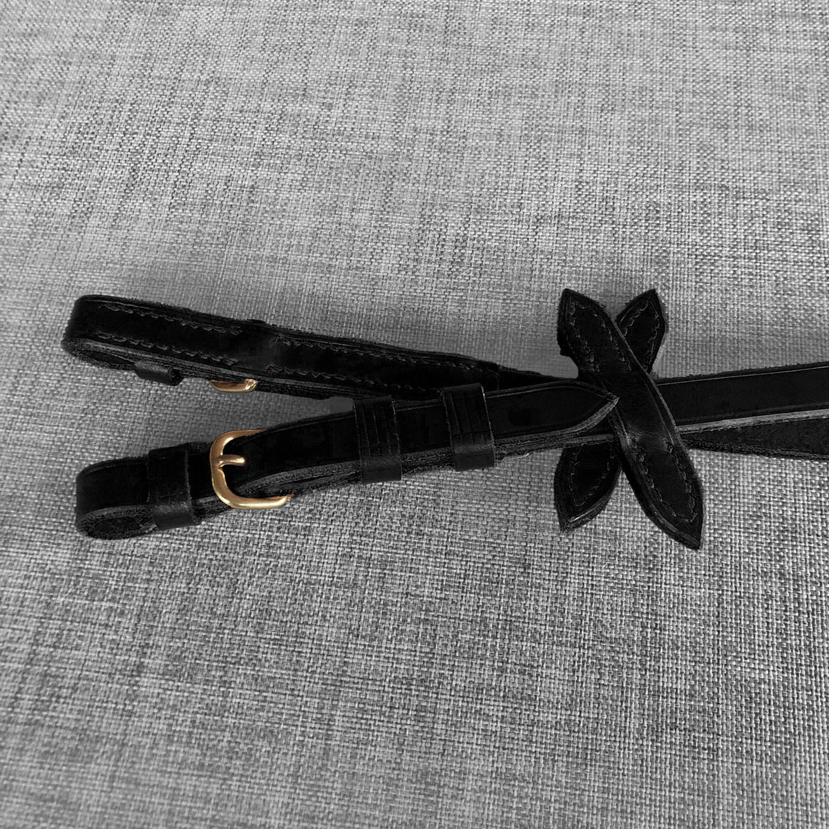 Detail de la boucle doree et de l'arretoir en forme de feuille sur des renes en cuir noir