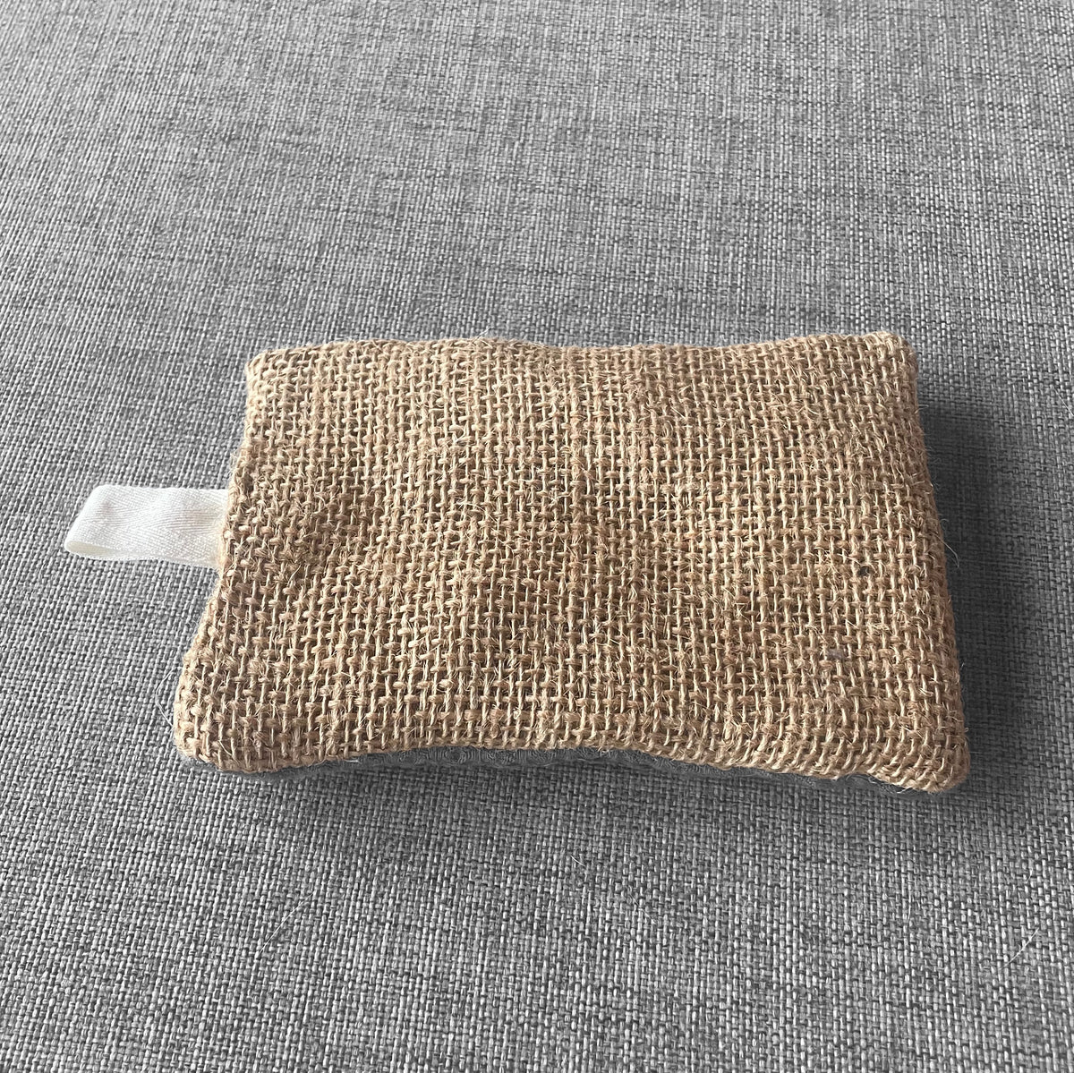Sachet en tissu de jute beige avec boucle en tissu blanc pose sur un fond gris