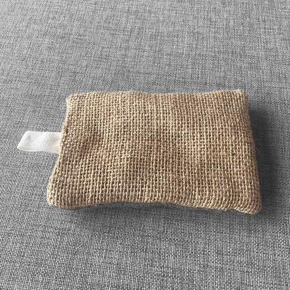 Sachet en tissu de jute beige avec boucle en tissu blanc pose sur un fond gris