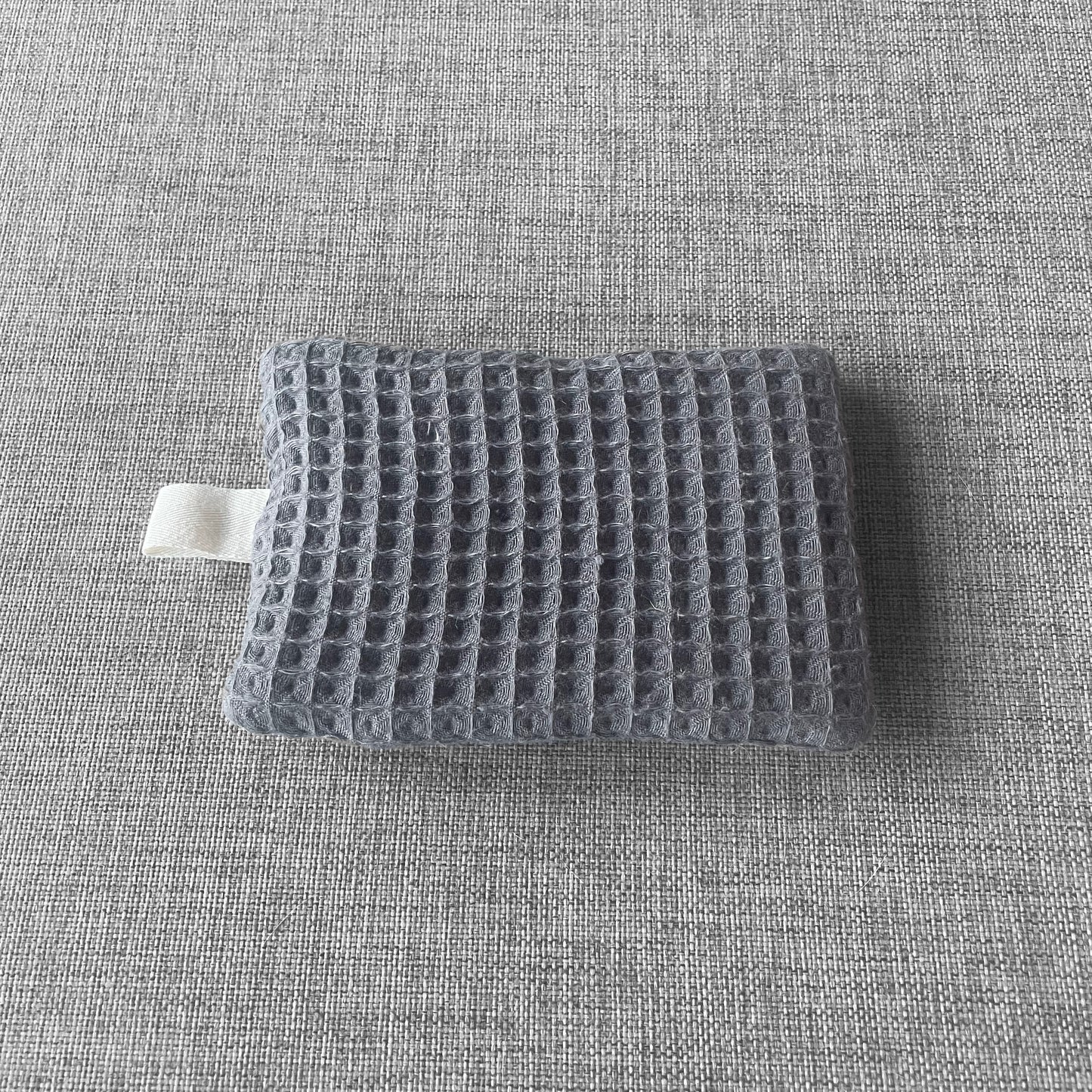 Sachet en tissu nid d'abeille gris avec boucle en tissu blanc pose sur un fond gris