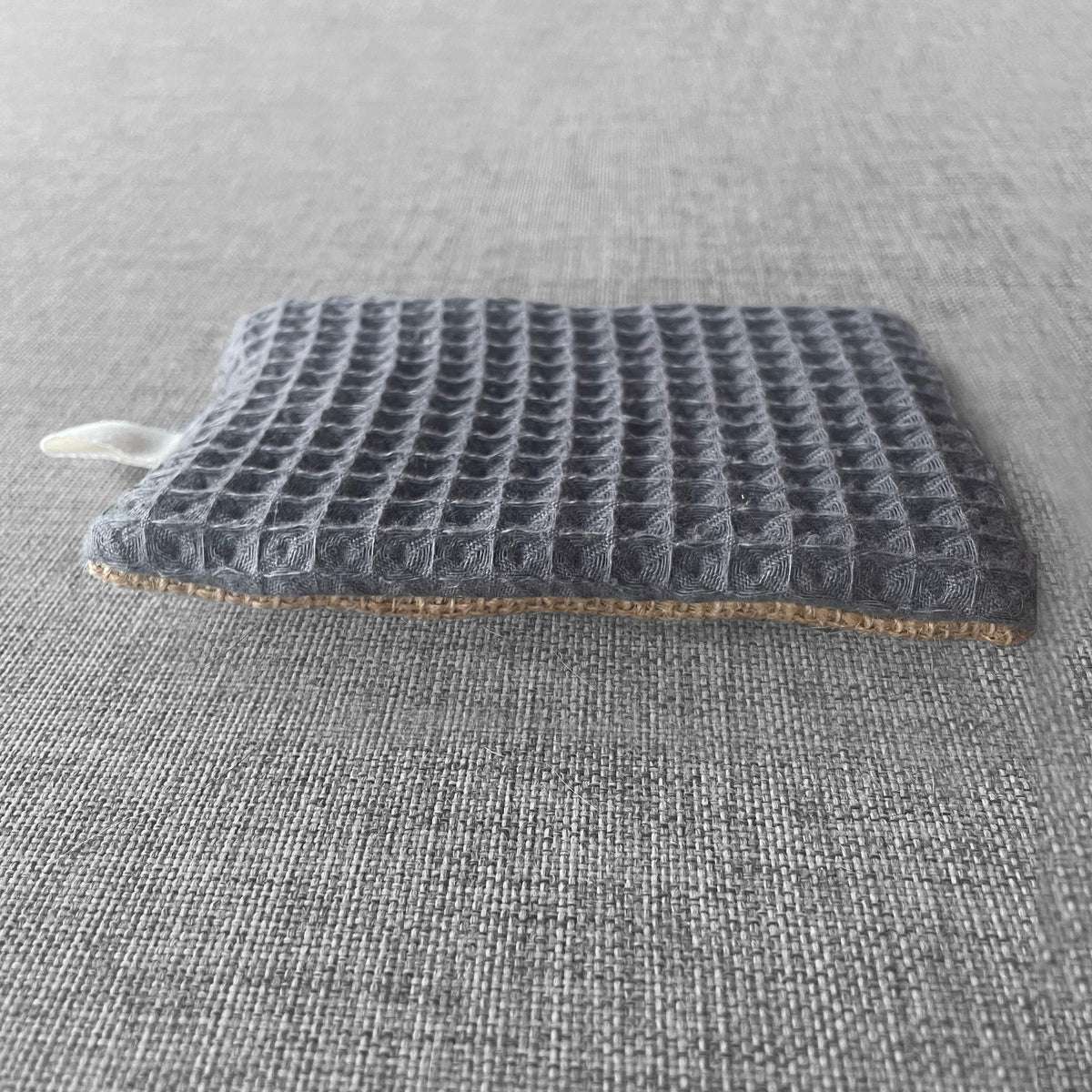 Sachet en tissu nid d'abeille gris avec doublure en jute pose sur un fond gris