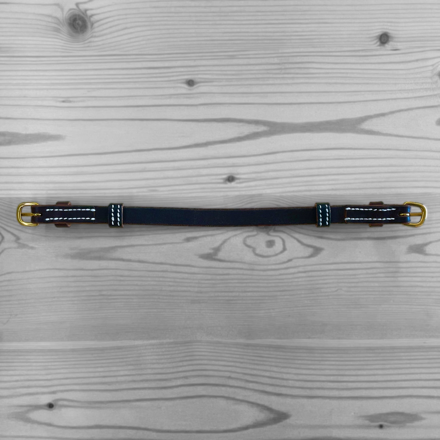 Sangle en cuir bleu marine avec couture blanche posee a plat sur un fond de bois