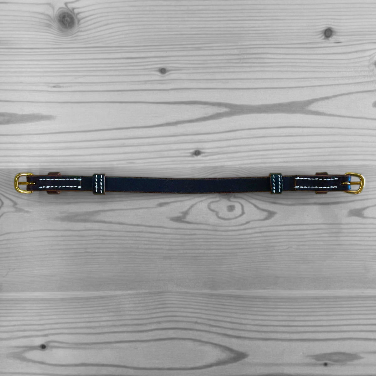 Sangle en cuir bleu marine avec couture blanche posee a plat sur un fond de bois