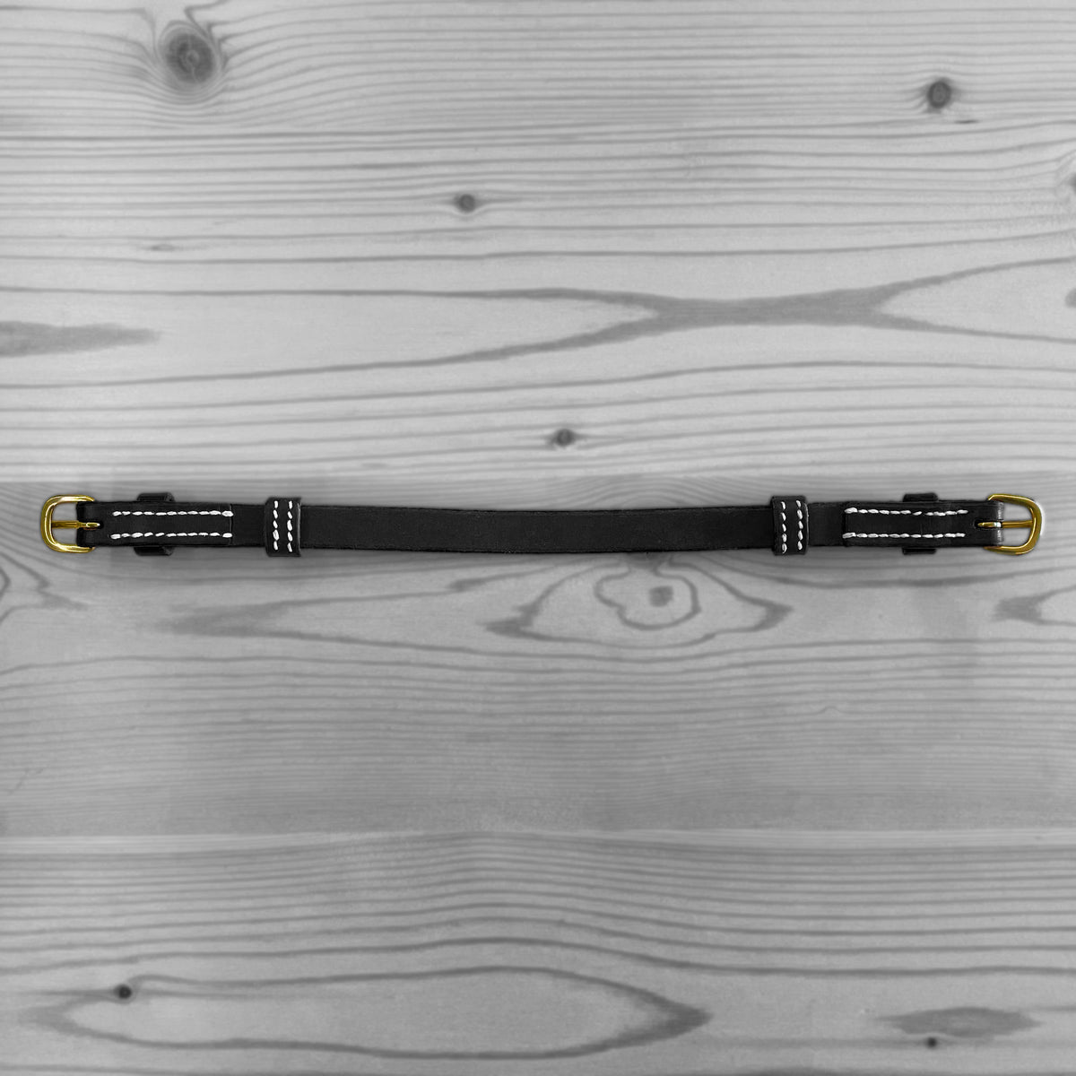 Sangle en cuir noir avec boucles metalliques posee a plat sur un fond de bois