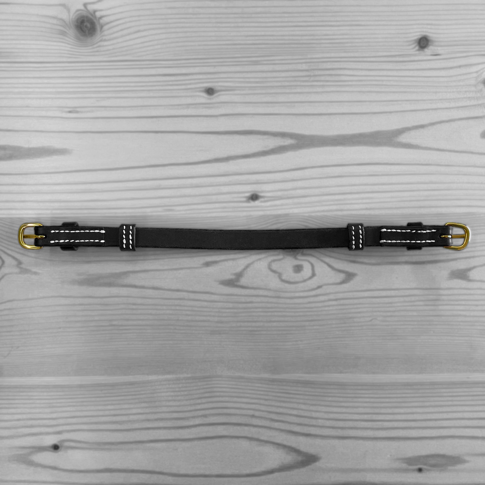 Sangle en cuir noir avec boucles metalliques posee a plat sur un fond de bois