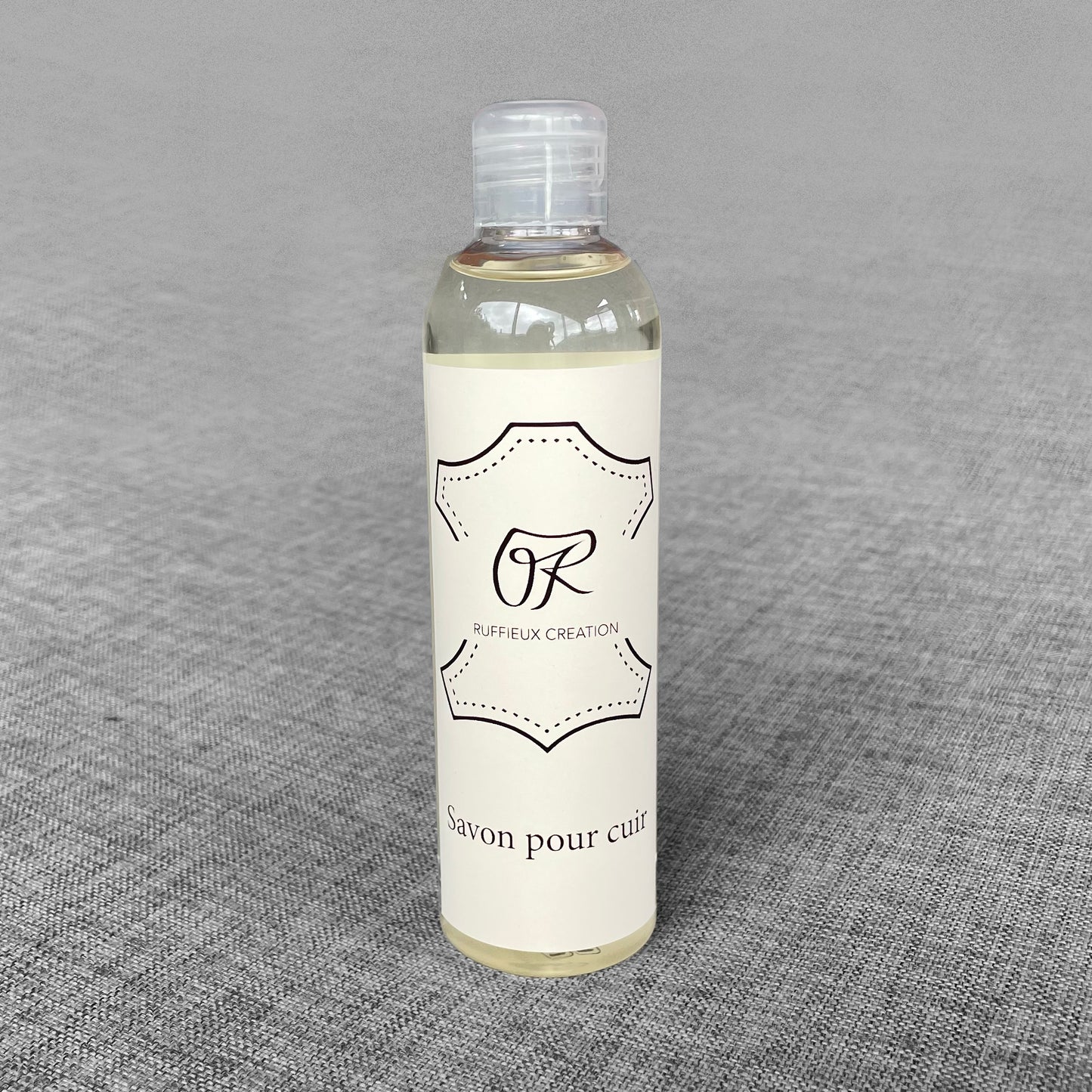 Flacon de savon pour cuir Ruffieux Creation pose sur un fond gris
